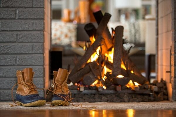 Brown duck boots sitting in front of a lit fireplace.