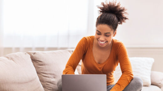 A woman works on a laptop on a couch.